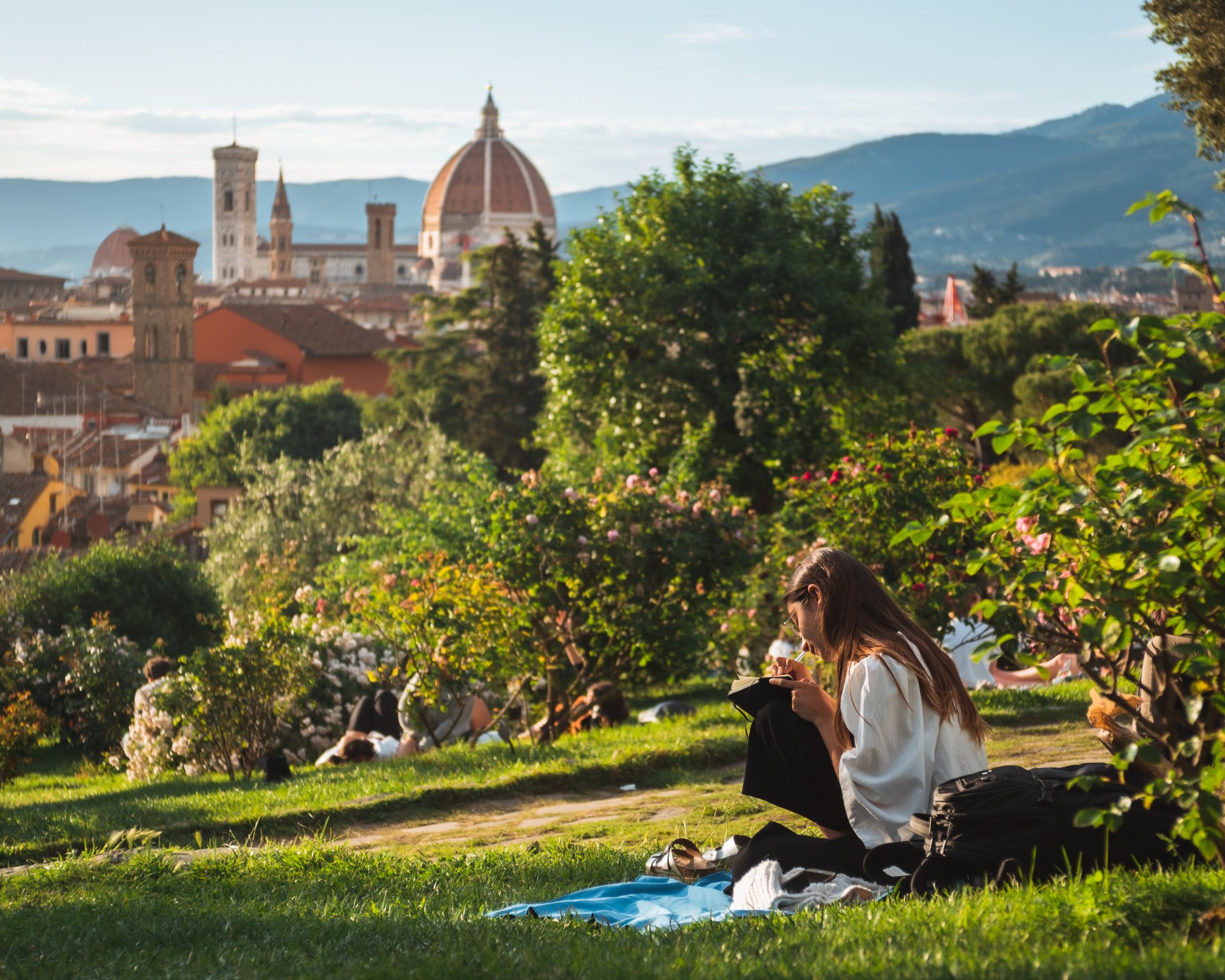 Fiatal nő olvas a füvön, háttérben Firenze látképe